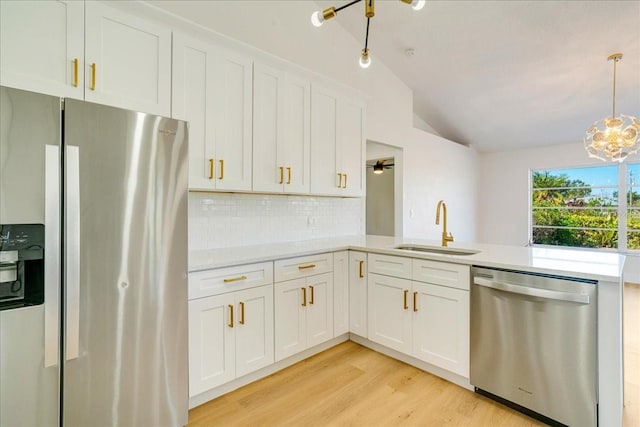 kitchen with appliances with stainless steel finishes, vaulted ceiling, sink, white cabinets, and hanging light fixtures