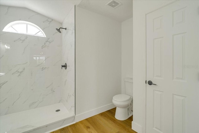 bathroom featuring a tile shower, hardwood / wood-style floors, and toilet