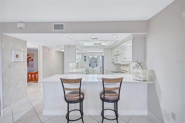 kitchen with white appliances, white cabinets, a kitchen breakfast bar, light tile patterned floors, and kitchen peninsula