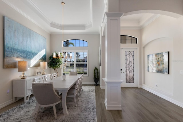 dining space featuring decorative columns, a raised ceiling, dark wood-type flooring, and ornamental molding