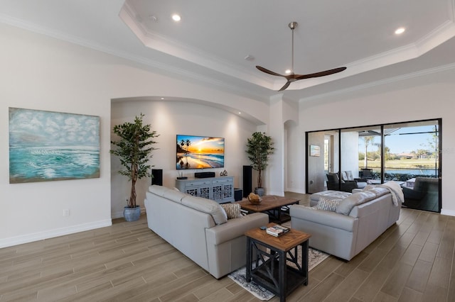 living room with light hardwood / wood-style floors, a tray ceiling, ornamental molding, and ceiling fan