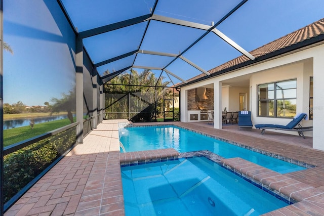 view of pool featuring an in ground hot tub, an outdoor kitchen, a water view, glass enclosure, and a patio