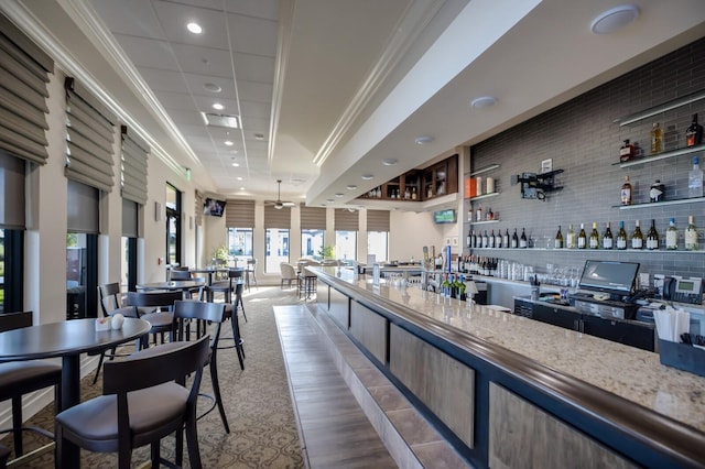 bar with backsplash, light stone countertops, hardwood / wood-style floors, and ornamental molding