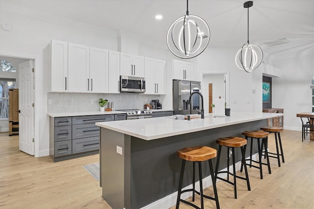 kitchen with white cabinetry, stainless steel appliances, light hardwood / wood-style floors, decorative light fixtures, and a kitchen island with sink