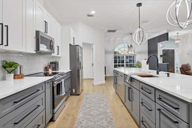 kitchen with stainless steel appliances, pendant lighting, light hardwood / wood-style flooring, a chandelier, and white cabinetry