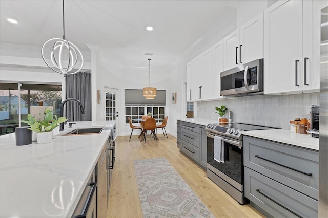 kitchen with appliances with stainless steel finishes, light wood-type flooring, sink, white cabinets, and hanging light fixtures