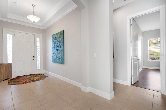 foyer with a raised ceiling, crown molding, baseboards, and light tile patterned floors