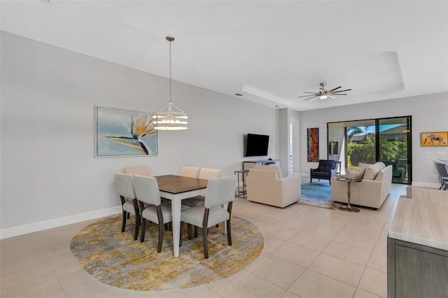 dining space featuring ceiling fan with notable chandelier, a tray ceiling, baseboards, and light tile patterned floors