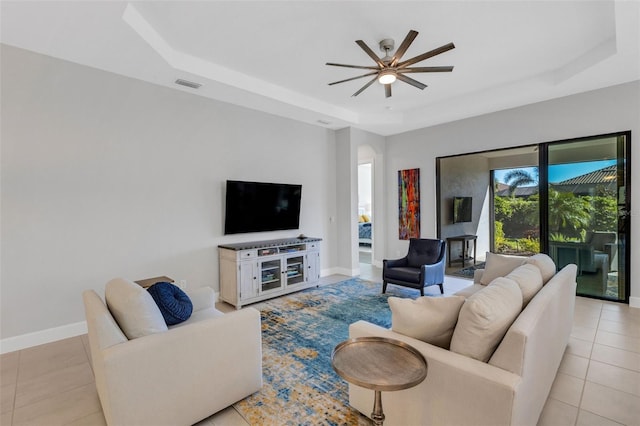 living room featuring a raised ceiling, visible vents, light tile patterned flooring, ceiling fan, and baseboards