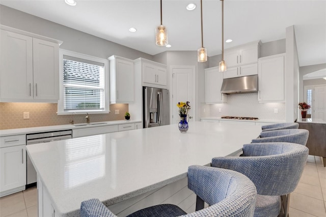 kitchen with a kitchen island, stainless steel appliances, light countertops, under cabinet range hood, and a sink