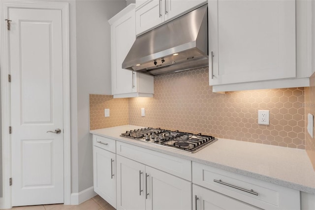 kitchen with stainless steel gas cooktop, backsplash, white cabinets, light tile patterned flooring, and under cabinet range hood