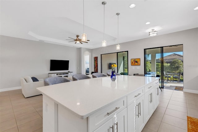 kitchen featuring a center island, a raised ceiling, hanging light fixtures, light tile patterned flooring, and baseboards