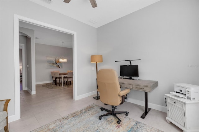 home office featuring a ceiling fan, arched walkways, baseboards, and light tile patterned floors