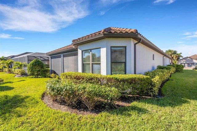 view of side of property featuring a yard, a tiled roof, and stucco siding