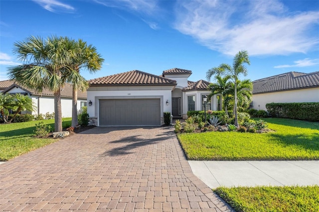 mediterranean / spanish house with a garage, a tile roof, decorative driveway, stucco siding, and a front lawn