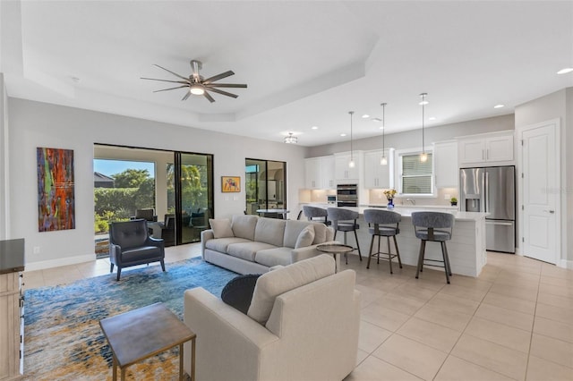 living area with light tile patterned floors, recessed lighting, a raised ceiling, a ceiling fan, and baseboards