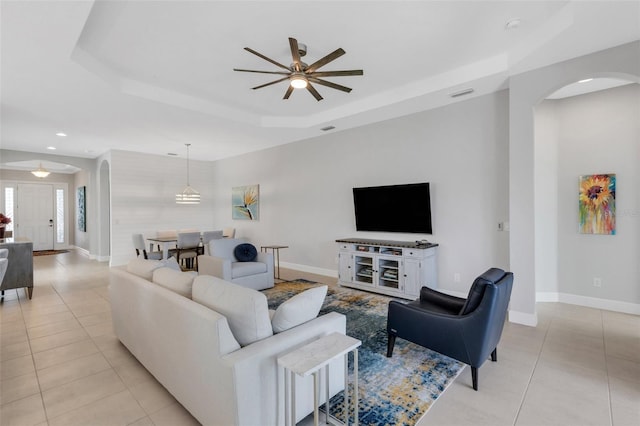 living area featuring arched walkways, visible vents, a tray ceiling, and light tile patterned floors