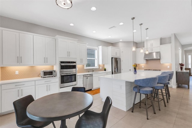 kitchen with under cabinet range hood, stainless steel appliances, white cabinetry, a healthy amount of sunlight, and a center island