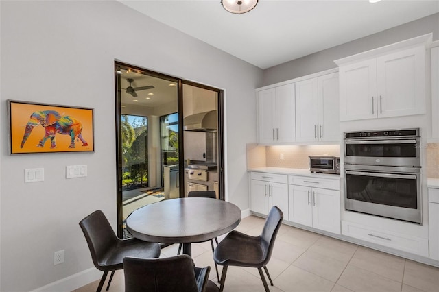 kitchen with backsplash, stainless steel double oven, white cabinets, light tile patterned flooring, and wall chimney range hood