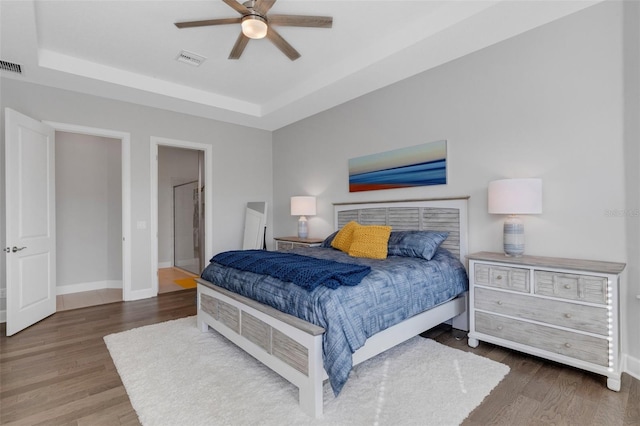 bedroom with a raised ceiling, visible vents, baseboards, and wood finished floors