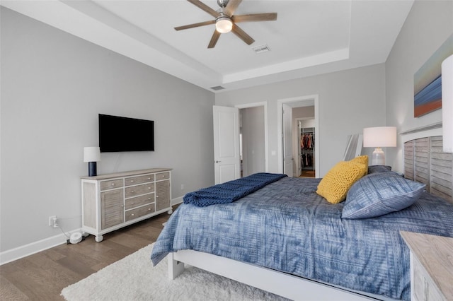 bedroom with wood finished floors, a raised ceiling, visible vents, and baseboards