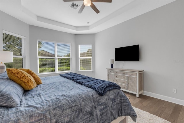 bedroom with baseboards, visible vents, a ceiling fan, a raised ceiling, and wood finished floors