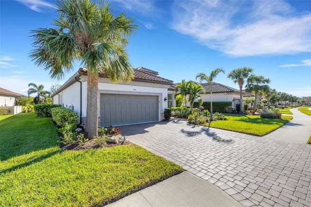 mediterranean / spanish-style house featuring a garage, decorative driveway, a front yard, and stucco siding