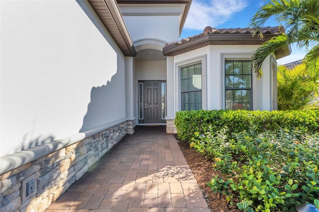 property entrance featuring a tiled roof, stone siding, and stucco siding