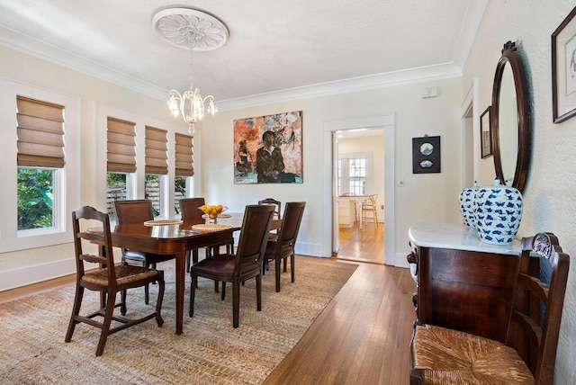 dining space featuring a textured ceiling, light wood-type flooring, ornamental molding, and an inviting chandelier