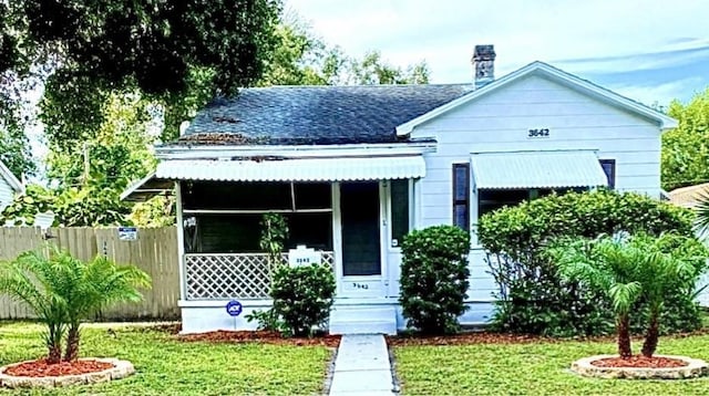 view of front of house with covered porch, a shingled roof, fence, a chimney, and a front yard