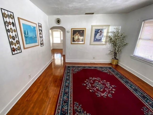 hallway with baseboards, visible vents, arched walkways, and wood finished floors