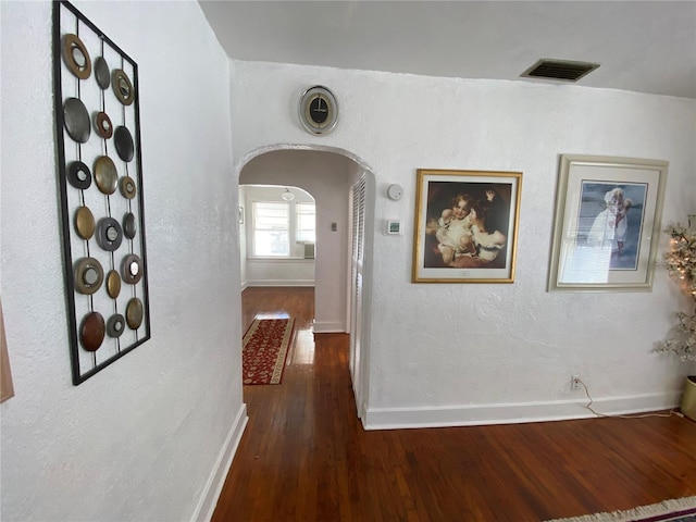 hallway featuring arched walkways, wood finished floors, visible vents, and baseboards