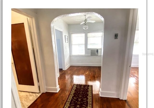 corridor featuring arched walkways, cooling unit, dark wood finished floors, and baseboards