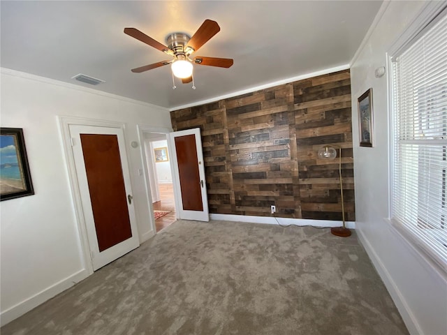 unfurnished room with wood walls, visible vents, baseboards, ornamental molding, and carpet