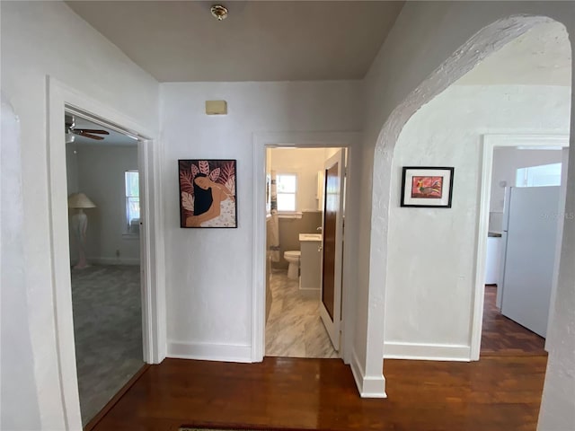 hallway featuring baseboards, arched walkways, and wood finished floors