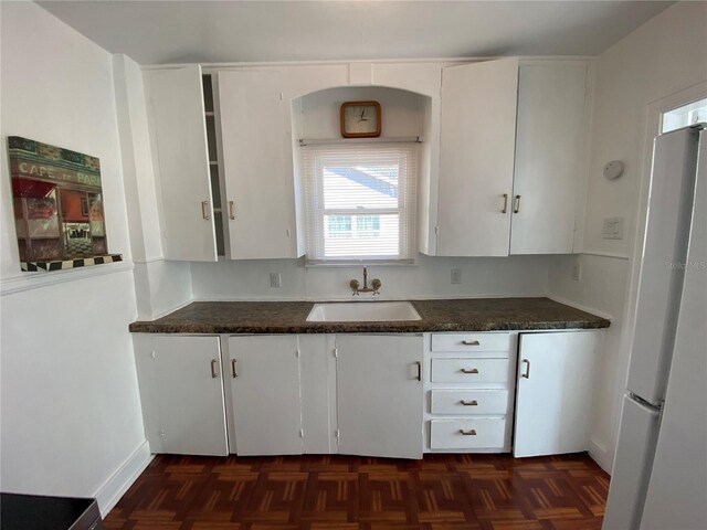 kitchen featuring freestanding refrigerator, white cabinetry, a sink, and dark countertops