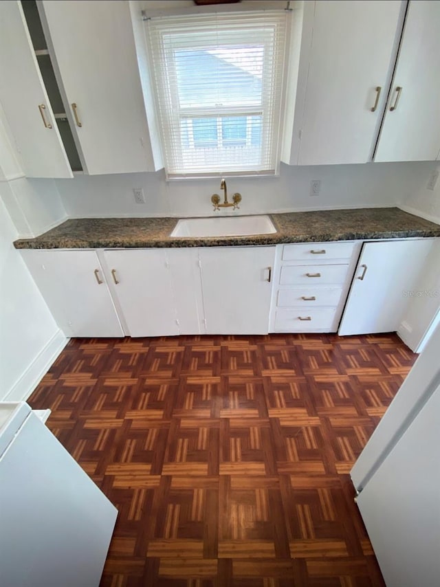 kitchen with white cabinetry, dark stone counters, and a sink