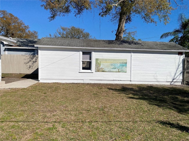 rear view of property featuring roof with shingles, a lawn, and fence