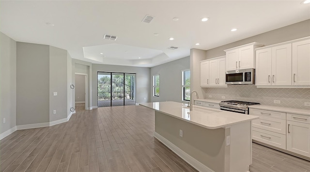 kitchen with sink, light wood-type flooring, an island with sink, white cabinetry, and stainless steel appliances