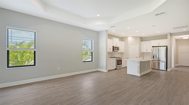 kitchen featuring appliances with stainless steel finishes, a center island with sink, white cabinetry, and light hardwood / wood-style floors