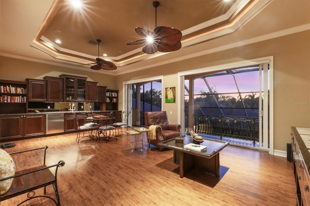 living room with a tray ceiling, ornamental molding, and light wood-type flooring