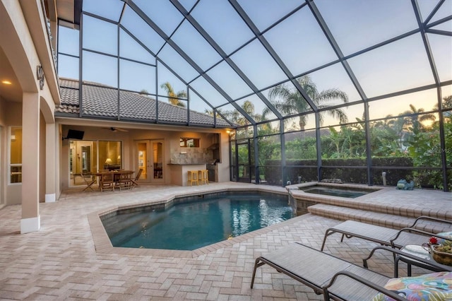 pool at dusk featuring an in ground hot tub, a patio, and glass enclosure