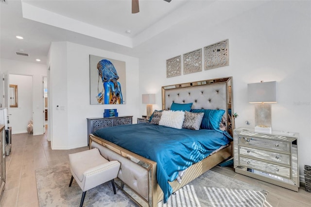 bedroom featuring a tray ceiling, ceiling fan, and light wood-type flooring