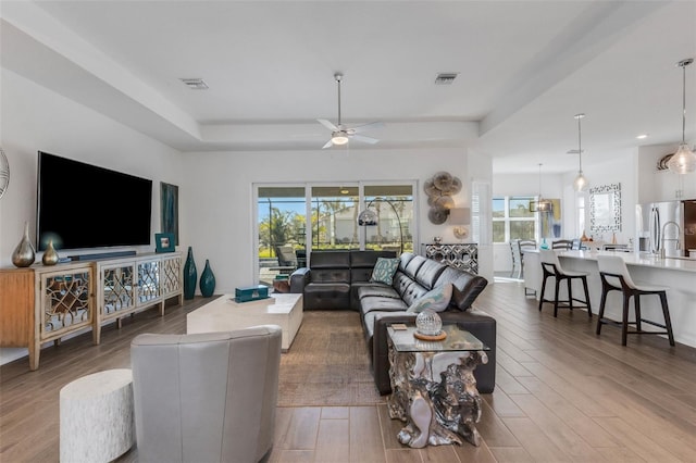 living room featuring ceiling fan, wood-type flooring, and a tray ceiling