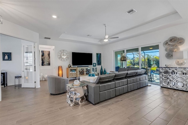 living room featuring a tray ceiling, light hardwood / wood-style flooring, and ceiling fan