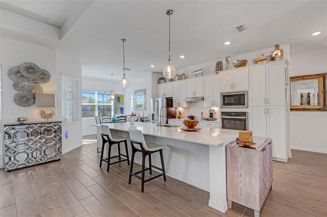 kitchen with built in microwave, a spacious island, white cabinets, oven, and hanging light fixtures