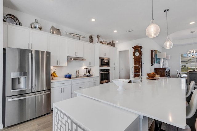 kitchen with white cabinets, a spacious island, hanging light fixtures, appliances with stainless steel finishes, and light hardwood / wood-style floors