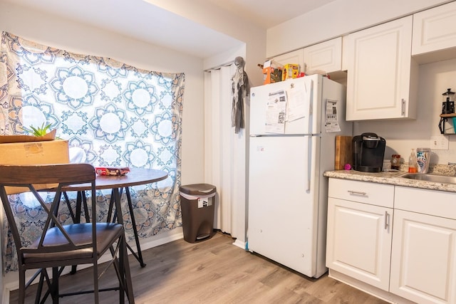 1038 25th St, Sarasota, FL 34234 - kitchen with freestanding refrigerator, light wood-type flooring, white cabinets, and light countertops