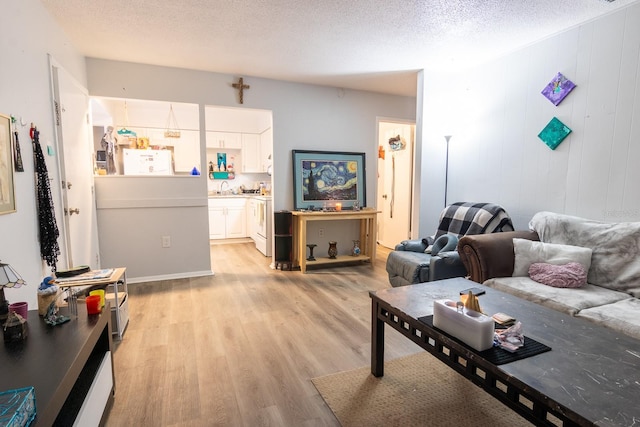 living room with a textured ceiling, light hardwood / wood-style flooring, wooden walls, and sink