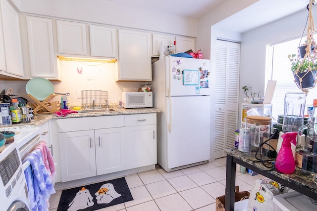 kitchen with white appliances, sink, light tile patterned flooring, white cabinetry, and washer / clothes dryer